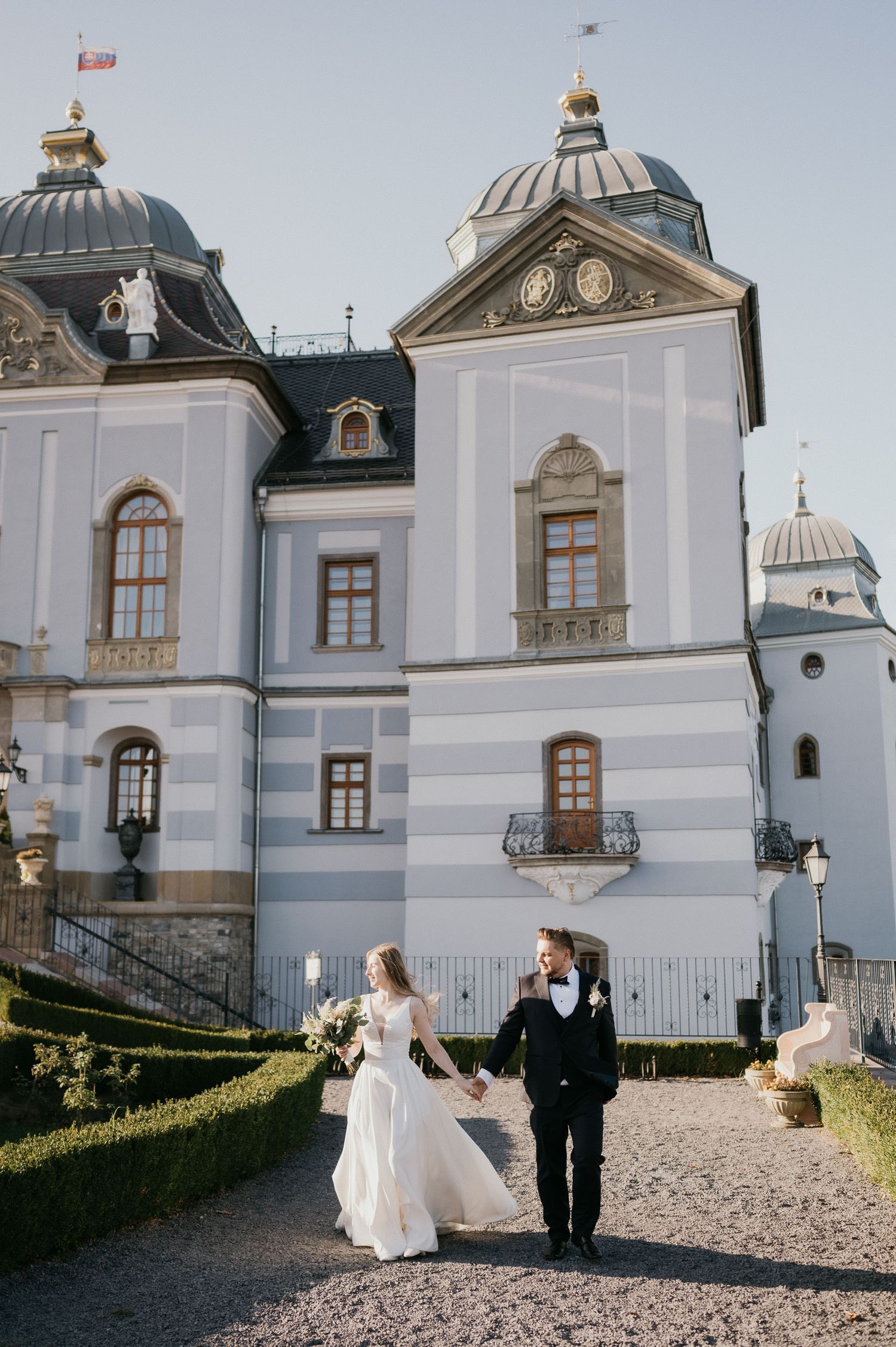Elegant white palace with domed towers serves as backdrop for wedding photos on a sunny day.