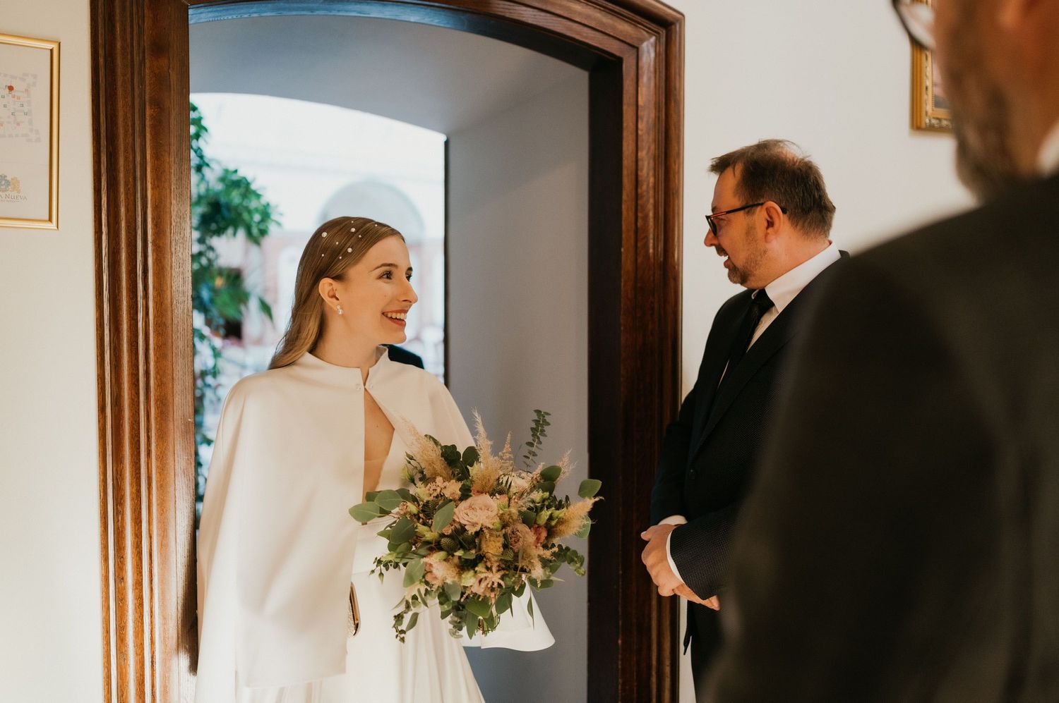 Wedding party gathered in a bright doorway with floral bouquet.