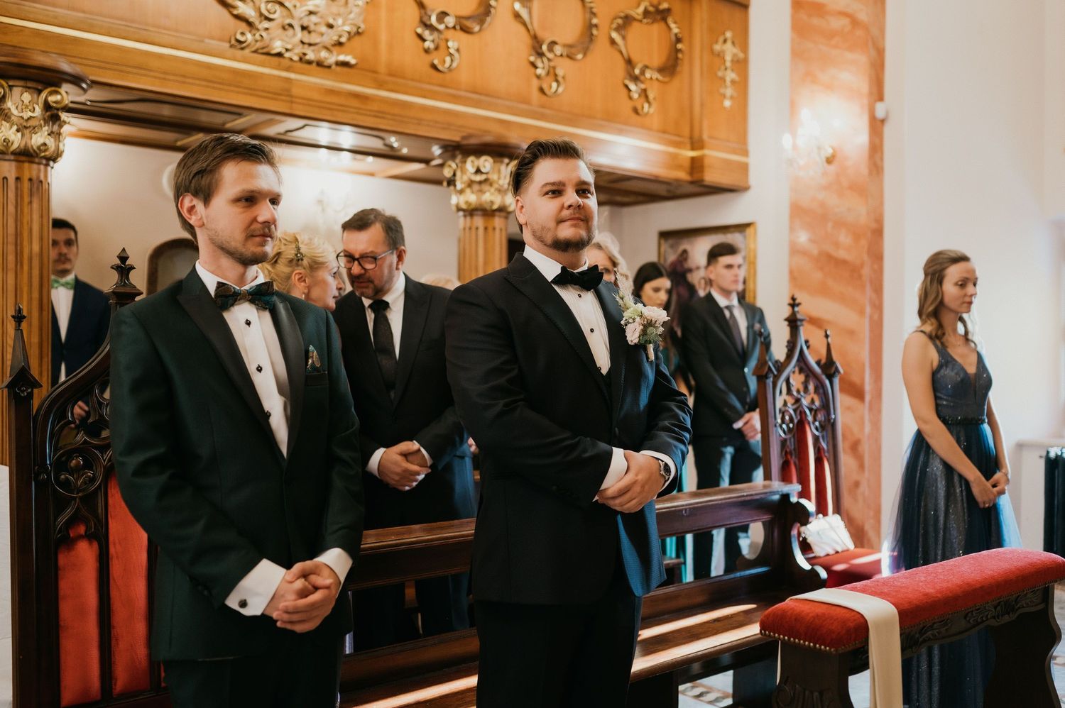Wedding guests in formal attire gathered in an elegant church interior.