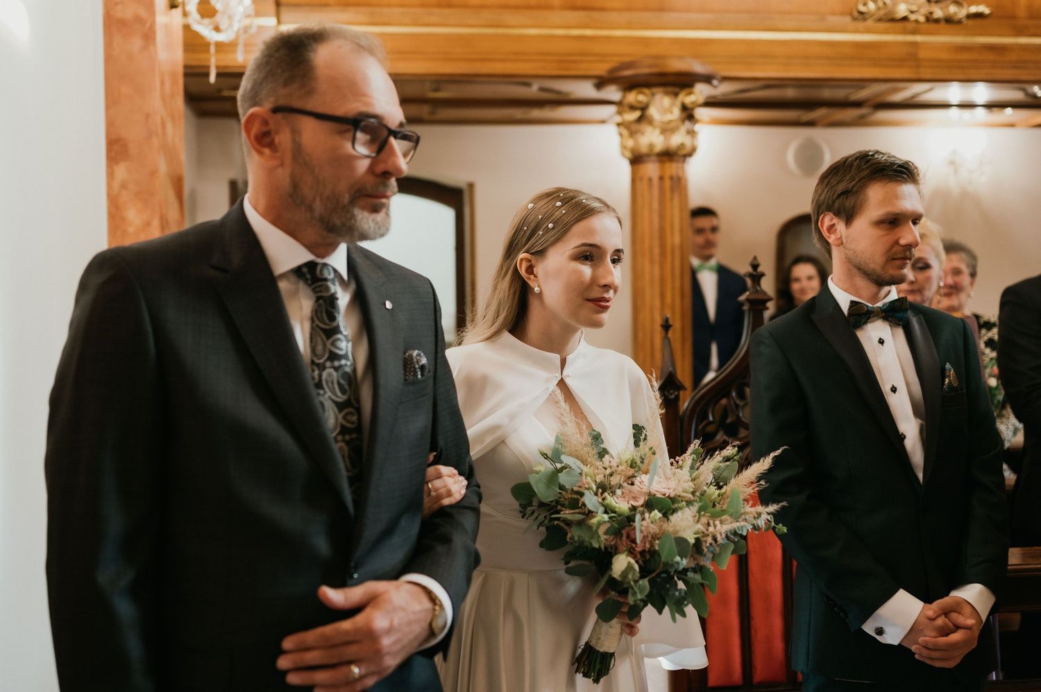 Wedding ceremony procession in an ornate church interior with wooden details.