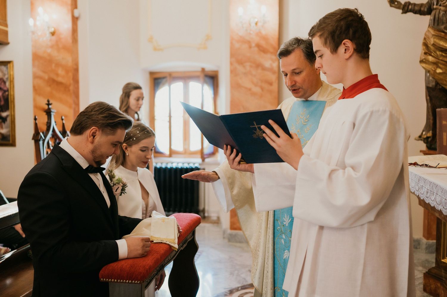 Wedding ceremony participants gather around a priest reading from a ceremonial book.