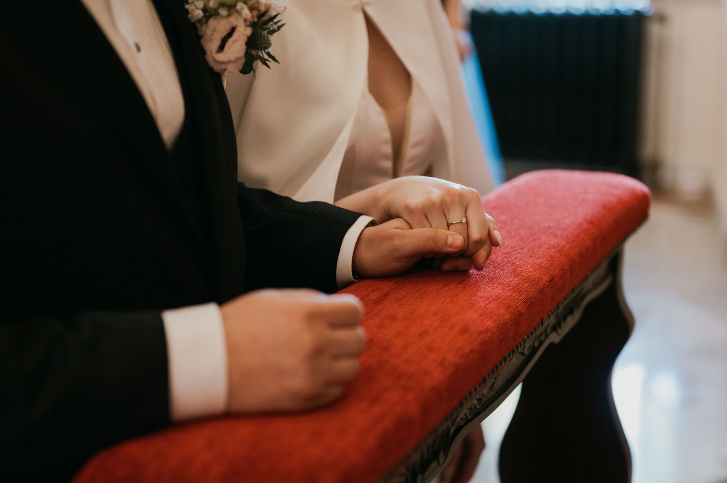Close-up of hands resting on a red church pew during a wedding ceremony.