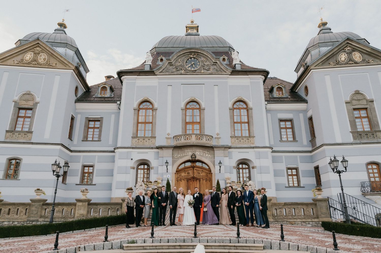 Elegant white baroque palace exterior with wedding party on grand steps.