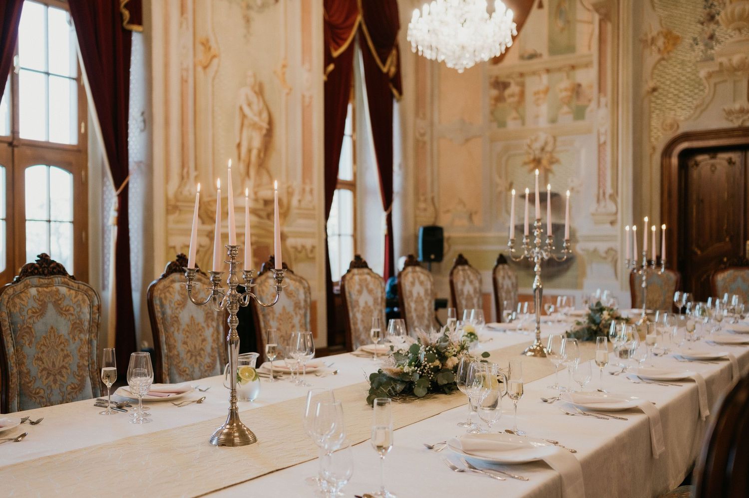Elegant table setting with candelabras and white linens in a luxurious dining room with ornate walls.