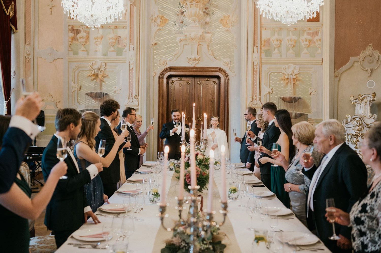Wedding celebration in an elegant dining room with guests seated at a long candlelit table.
