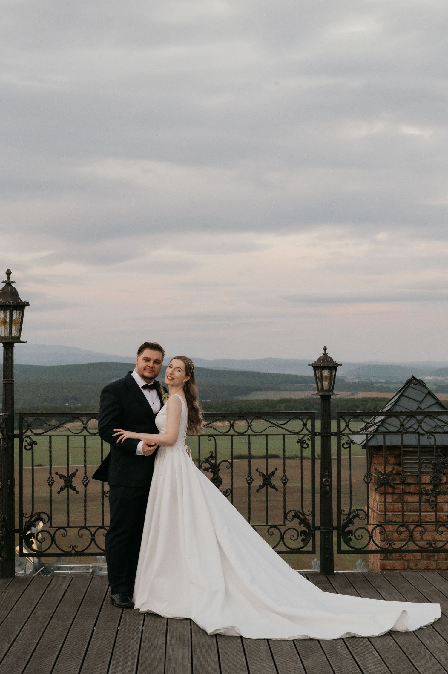 Newlyweds pose together on a deck overlooking mountains with classic lanterns and ornate iron railings.