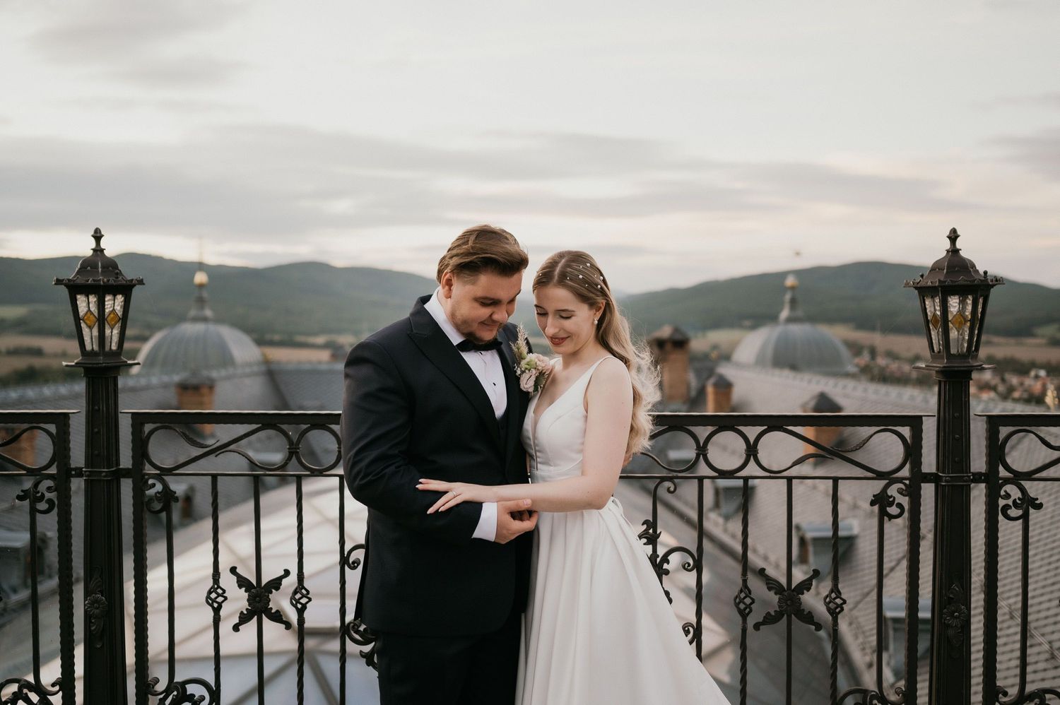 Wedding couple shares intimate moment on rustic balcony with vintage lamp posts and mountain views.