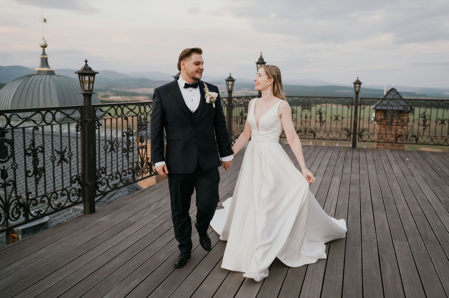 Wedding couple strolling on rustic deck with vintage lanterns and gorgeous mountain scenery.