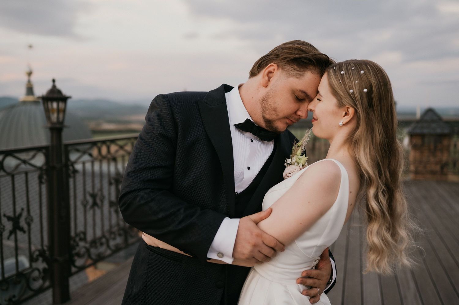 Romantic wedding couple share an intimate moment on a balcony overlooking mountains at sunset.