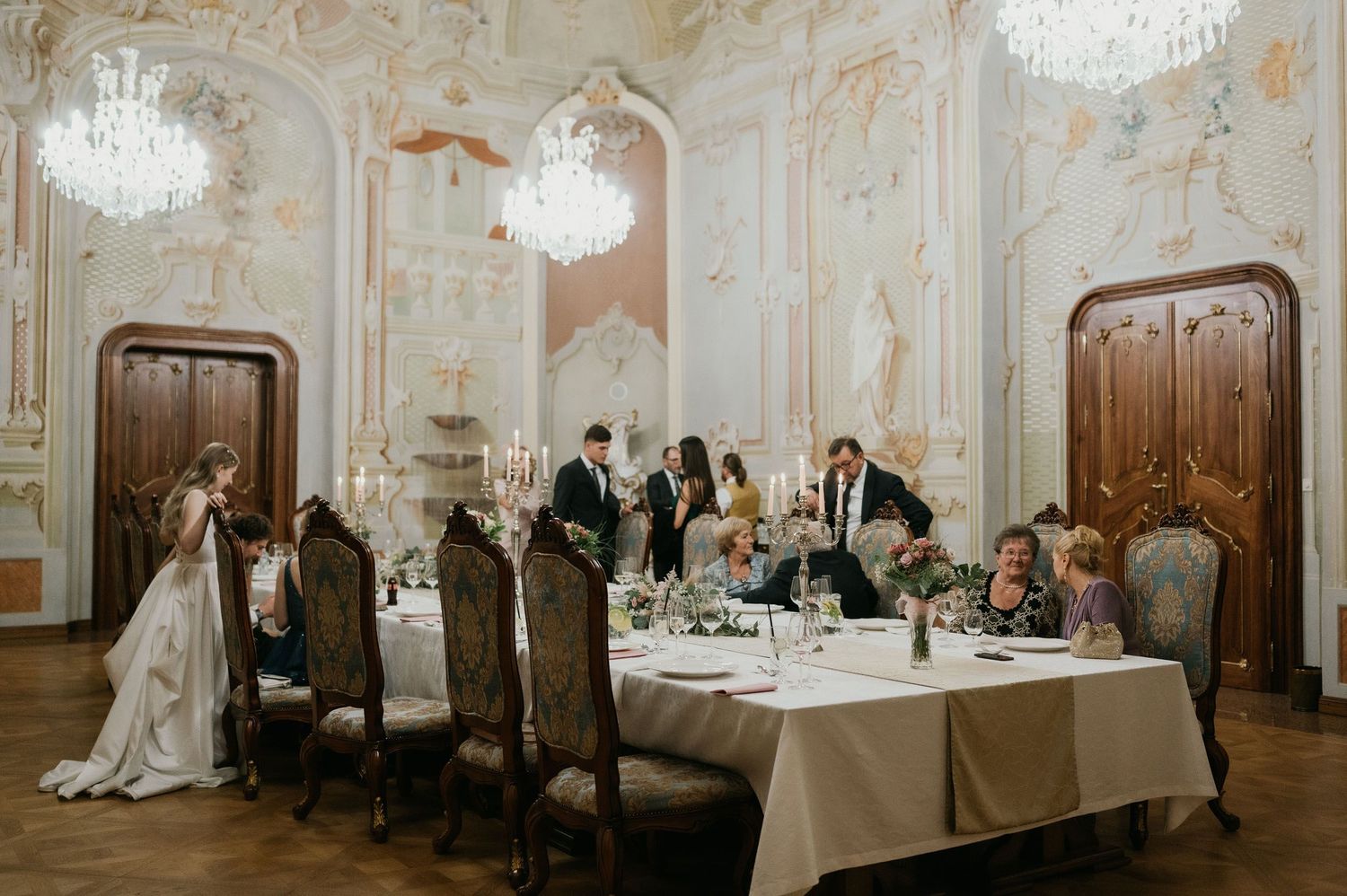 Wedding reception in an elegant baroque ballroom with crystal chandeliers and ornate decor.
