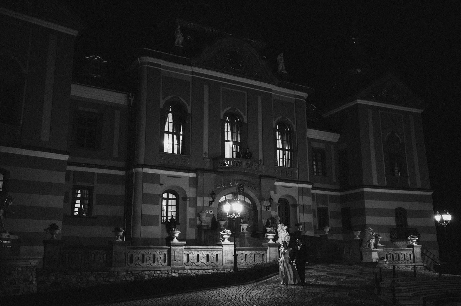 Black and white night portrait of wedding couple in front of historic building facade.