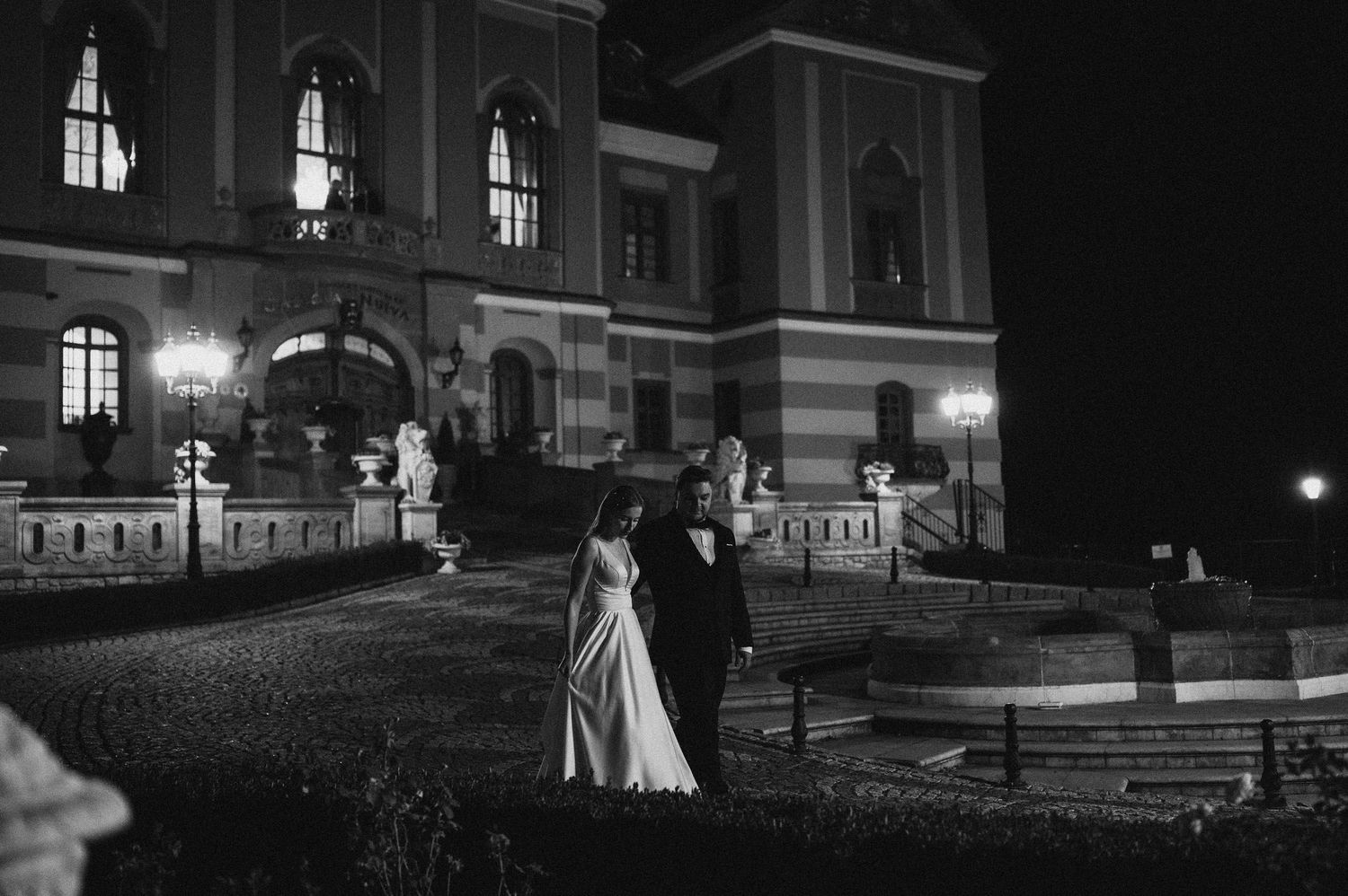 Dramatic nighttime wedding photo against illuminated classical architecture.