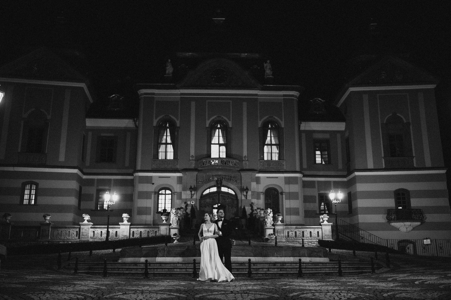 Elegant black and white wedding portrait in front of grand historic building at night.