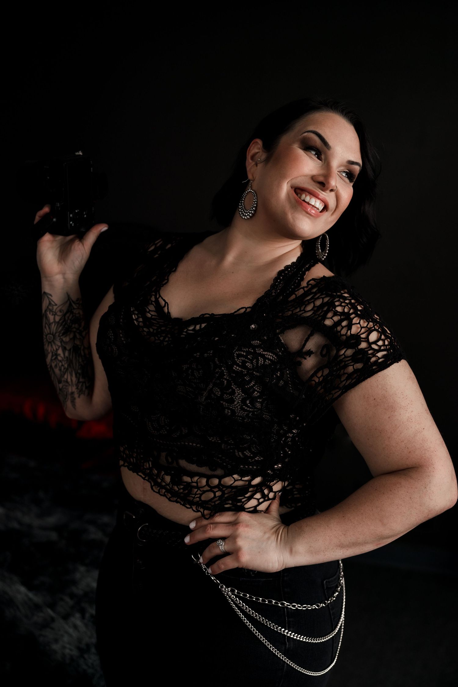 A boudoir photoshoot featuring black lace and dramatic lighting with silver chain accessories.