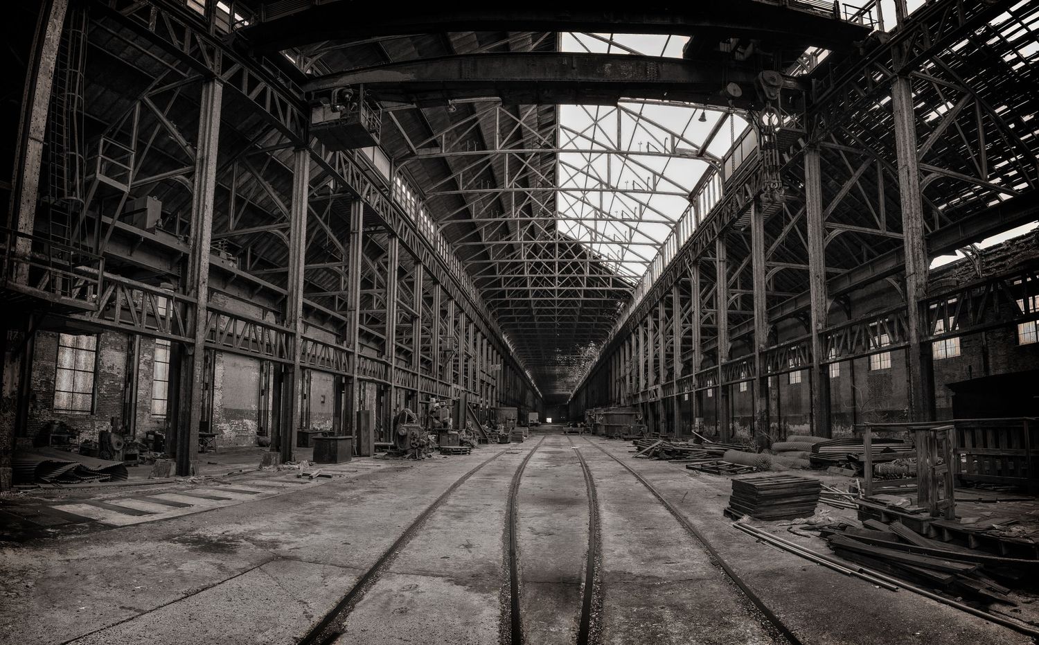 Abandoned industrial warehouse interior with railway tracks and dramatic ceiling architecture.