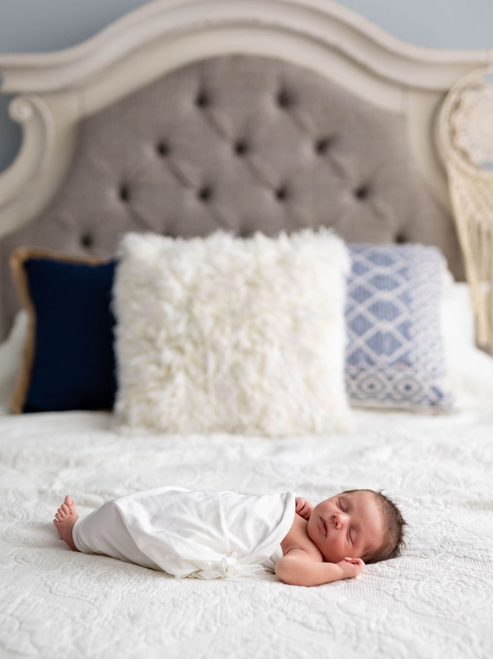 Newborn baby in white gown sleeping on elegant bed at Michele McCoy's photography studio in Mountain Home, AR.