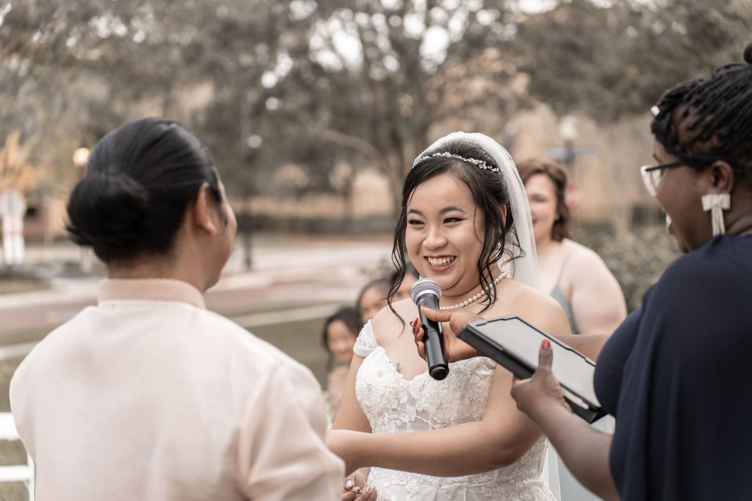 Bride in white dress smiles while speaking into microphone during wedding celebration.
