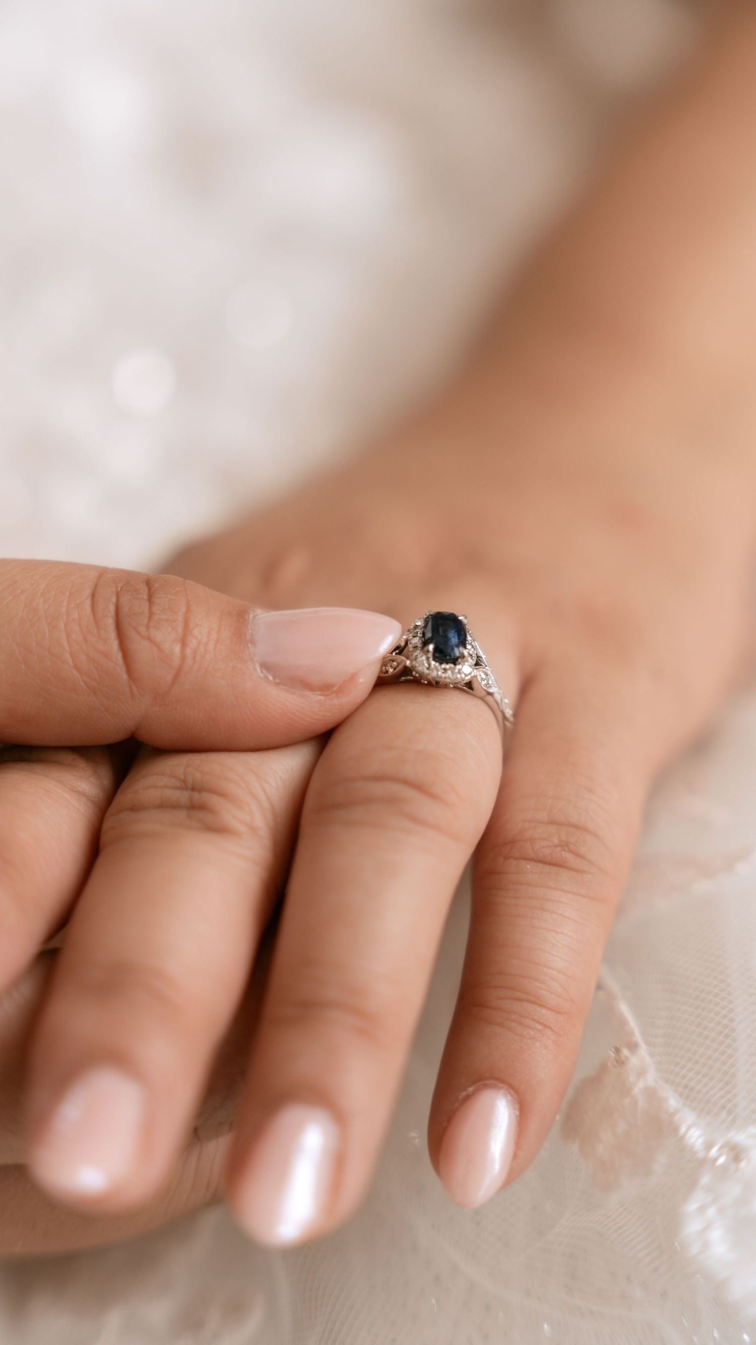 Close-up of elegant sapphire and diamond engagement ring on bride's manicured hand.