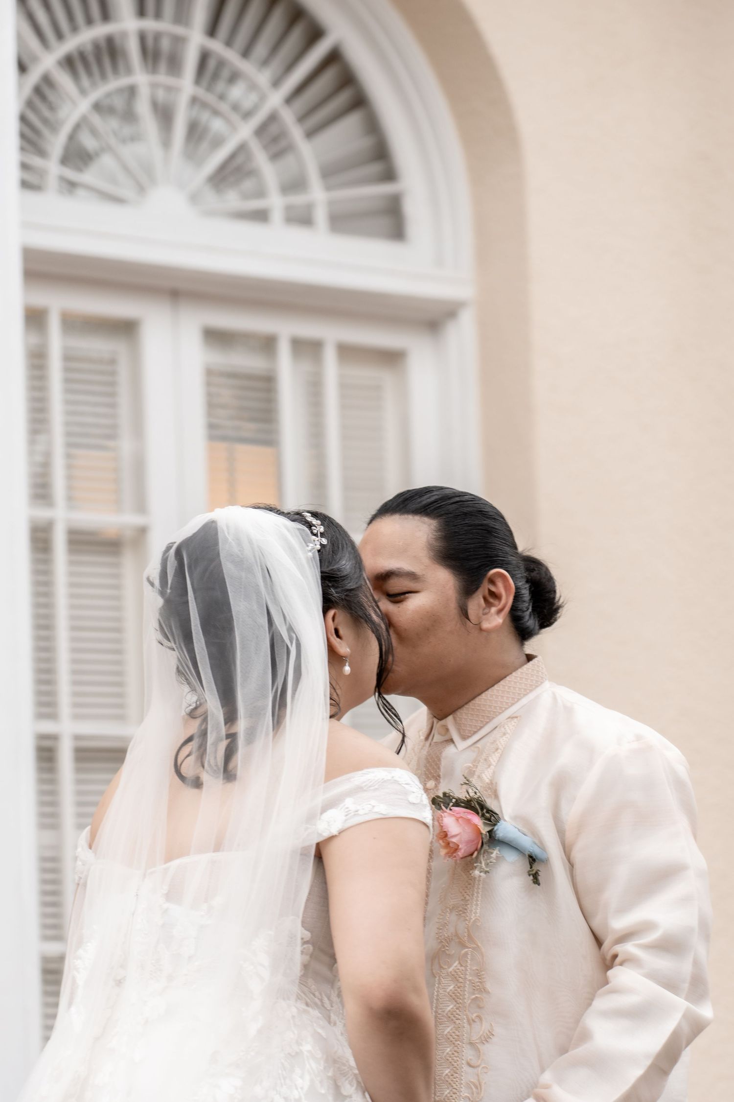 Romantic wedding couple sharing a kiss in front of elegant white colonial architecture.
