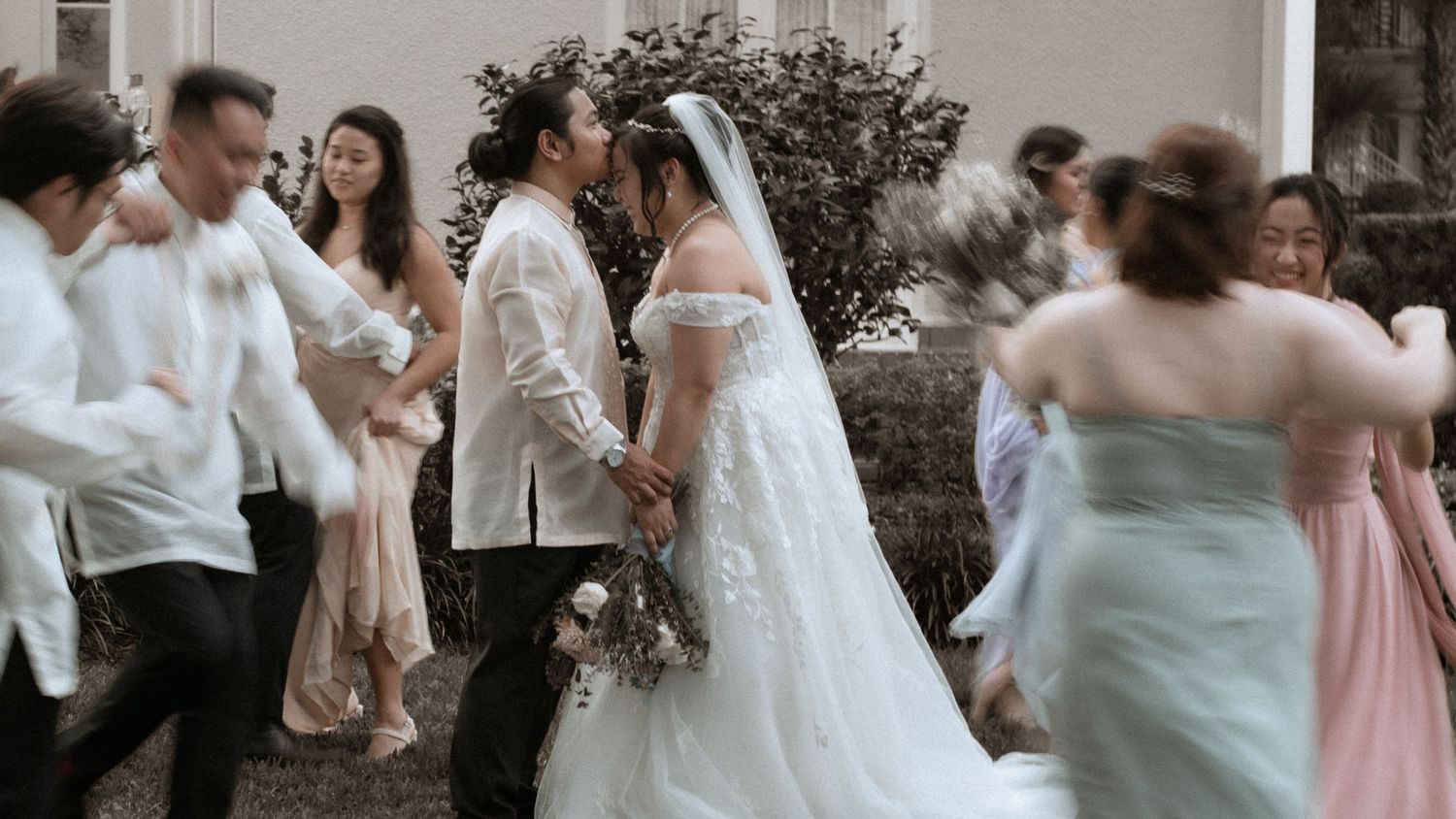Wedding celebration with couple surrounded by guests in white and pastel attire.