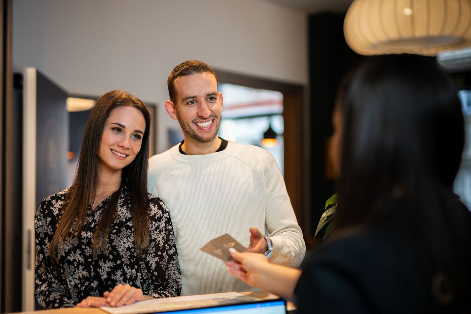 Fiatal pár érkezik a recepcióra – vendégfogadás jelenet lifestyle hangulattal, tökéletes szállásmarketinghez és brandépítéshez.
