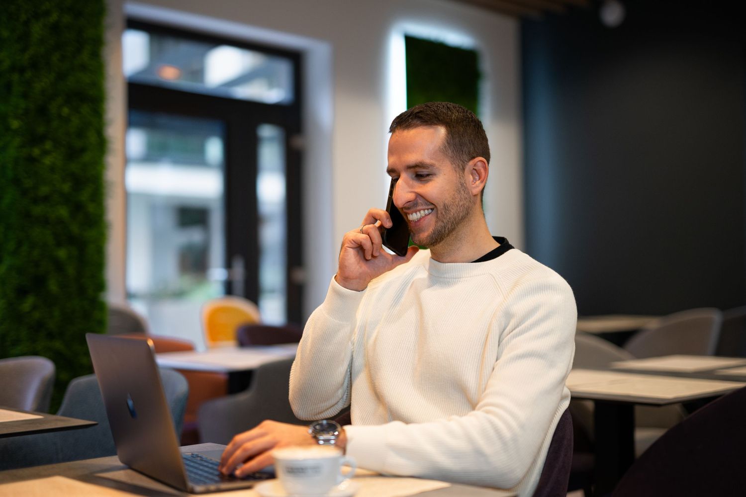 Üzleti portré laptop mellett, telefonáló férfival – coworking vagy hotel business corner fotó professzionális megjelenéshez.