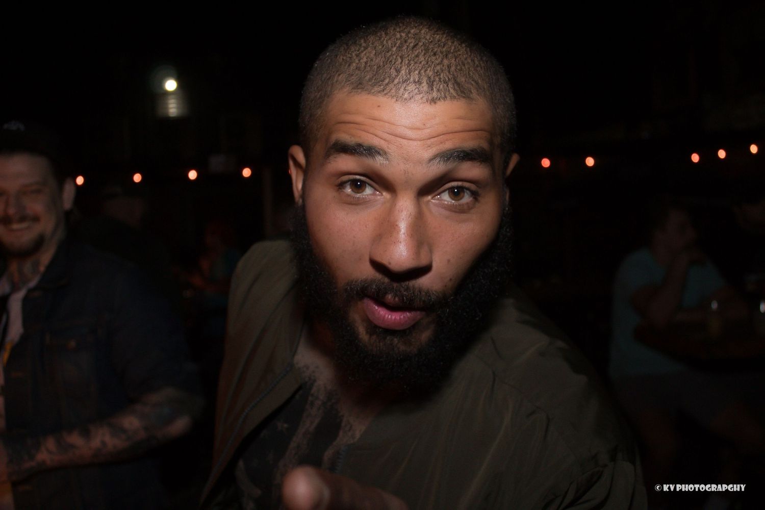 Close-up portrait of a tattooed man with short hair making a gesture at a nightclub event.