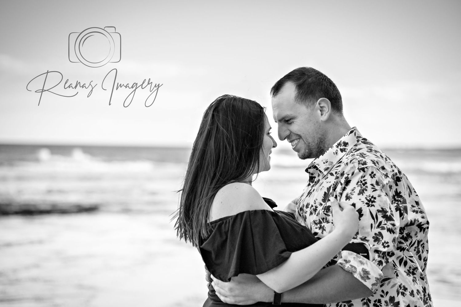 Black and white romantic couple embracing on a beach with ocean waves in the background.
