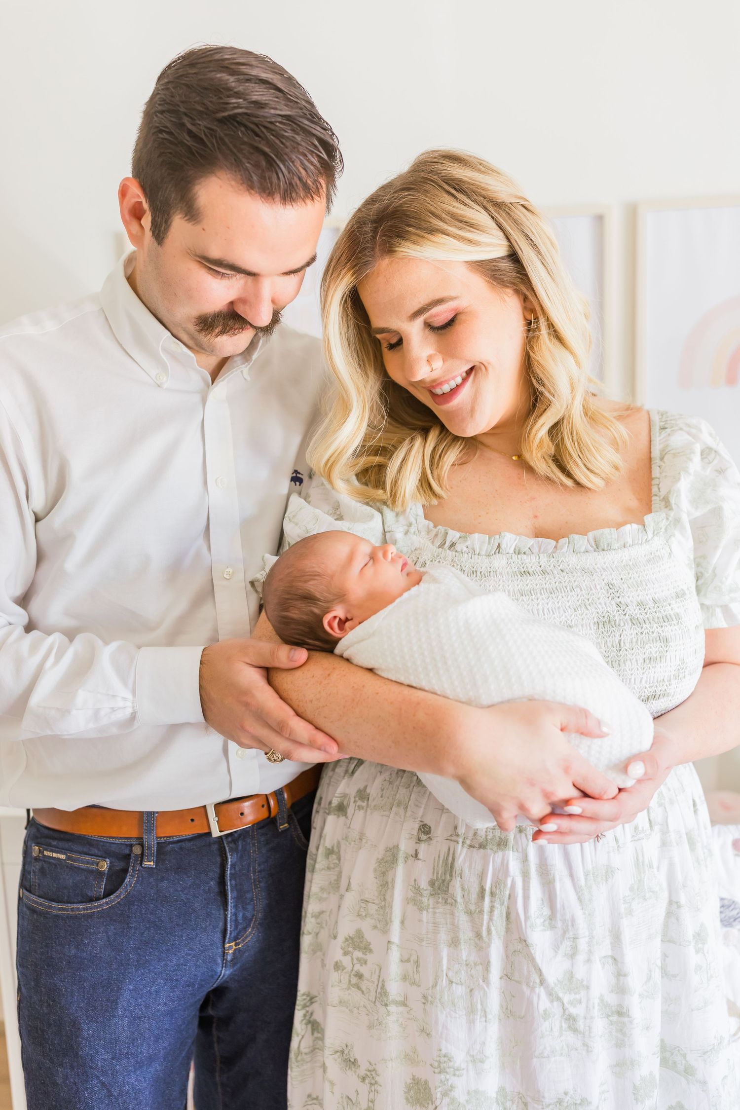 An intimate family portrait in a softly lit nursery with white and pastel decor.