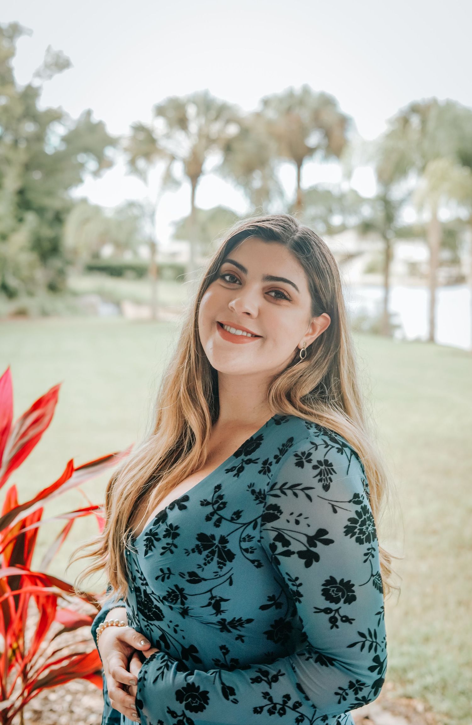 A woman in a floral dress poses outdoors against a palm tree backdrop.