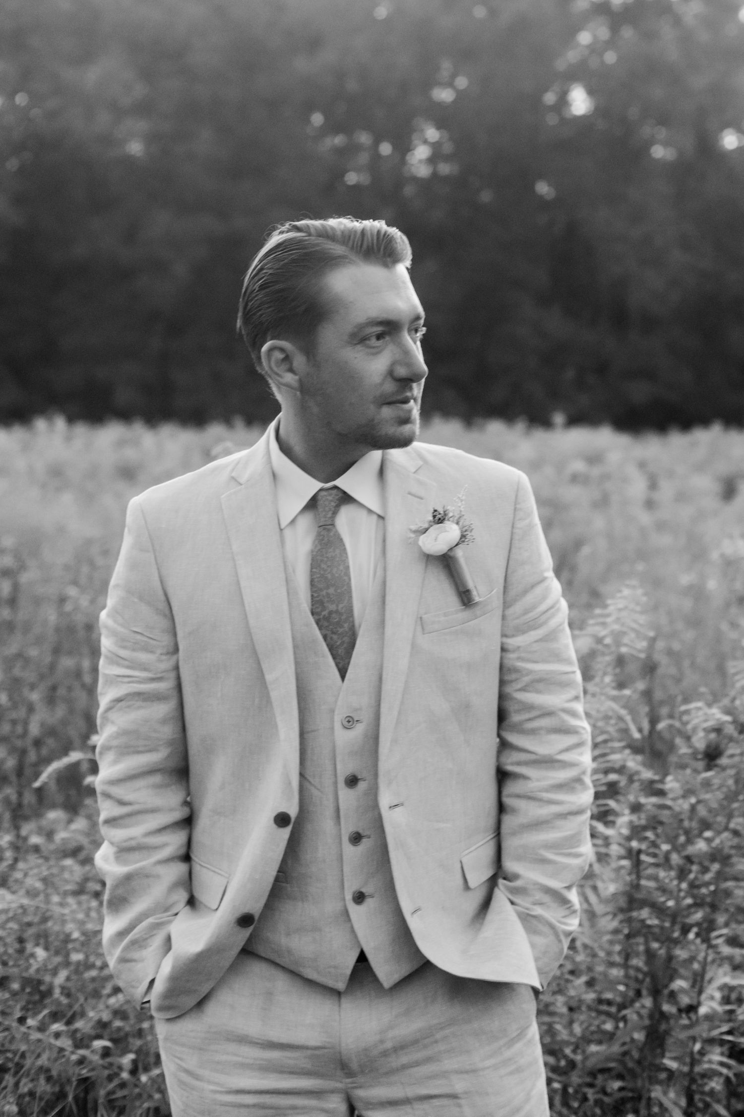 Groom in light gray three-piece suit poses in natural outdoor setting.