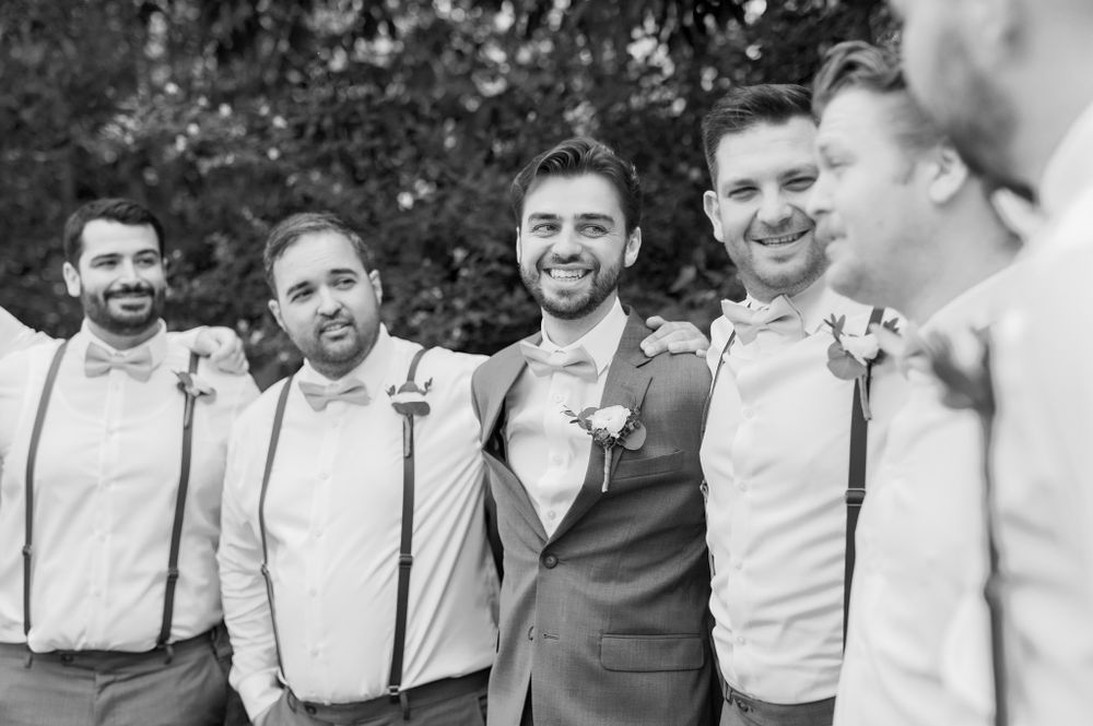 Groomsmen in suspenders and bowties pose together for wedding party photos.