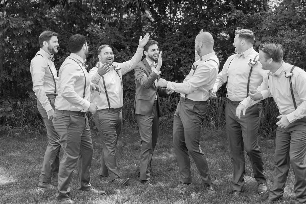Groomsmen in matching suspenders pose playfully for group photos outdoors.