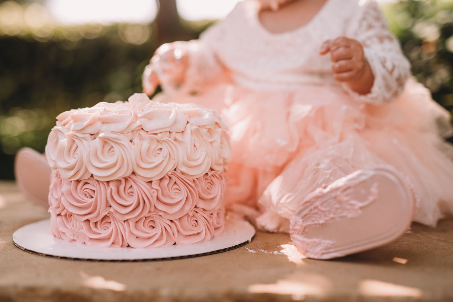 Pink rosette decorated cake next to tulle fabric in soft natural lighting.