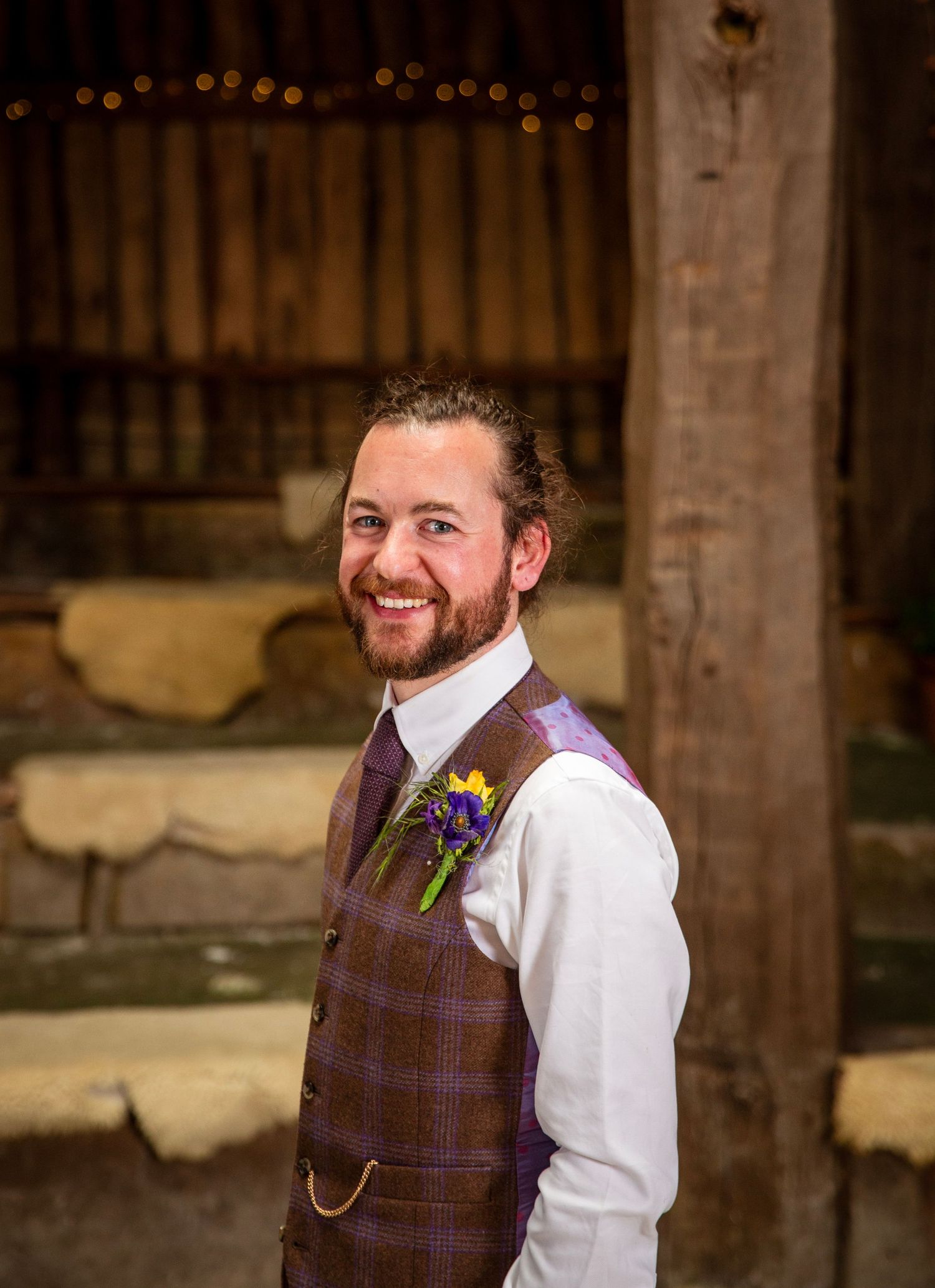 Person wearing purple plaid vest and white shirt at rustic wedding venue.