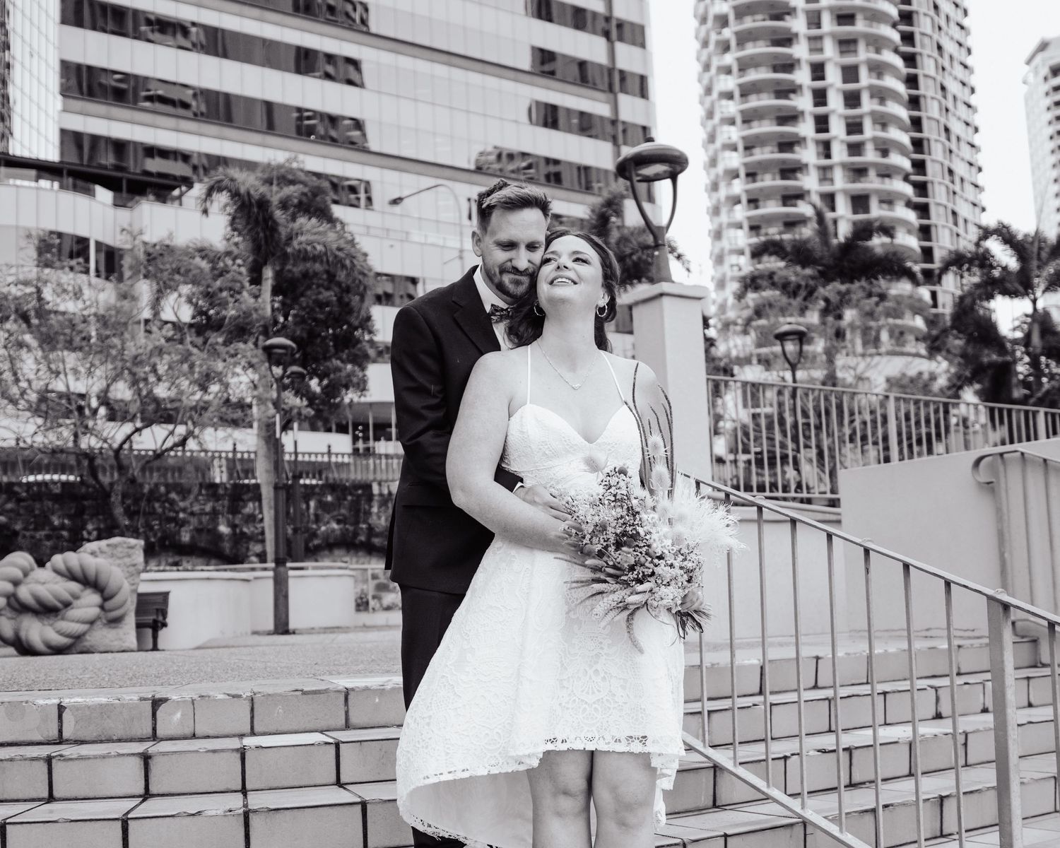A couple in wedding attire shares a joyful moment in an urban setting.