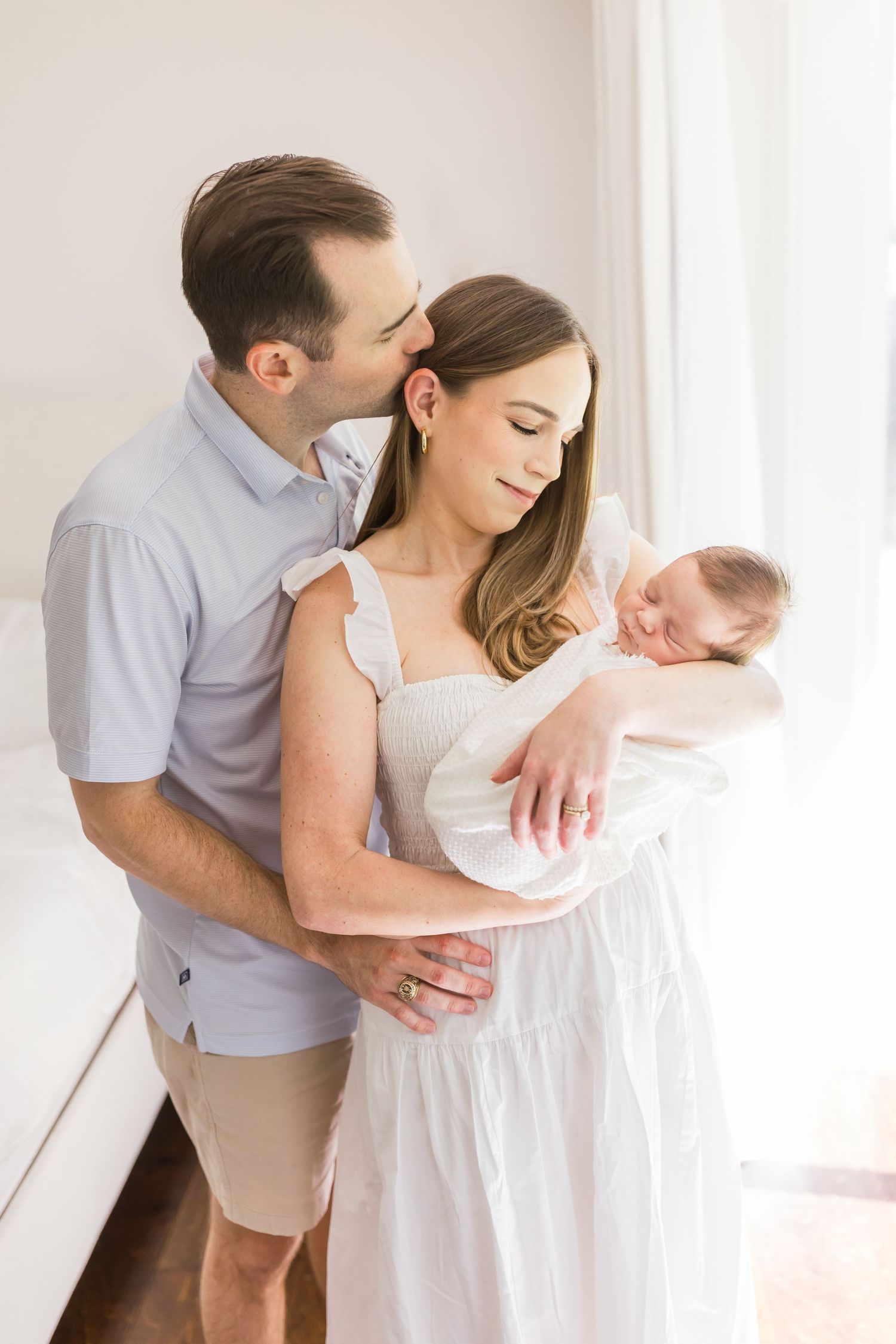 Intimate family moment with newborn baby by sunlit window.