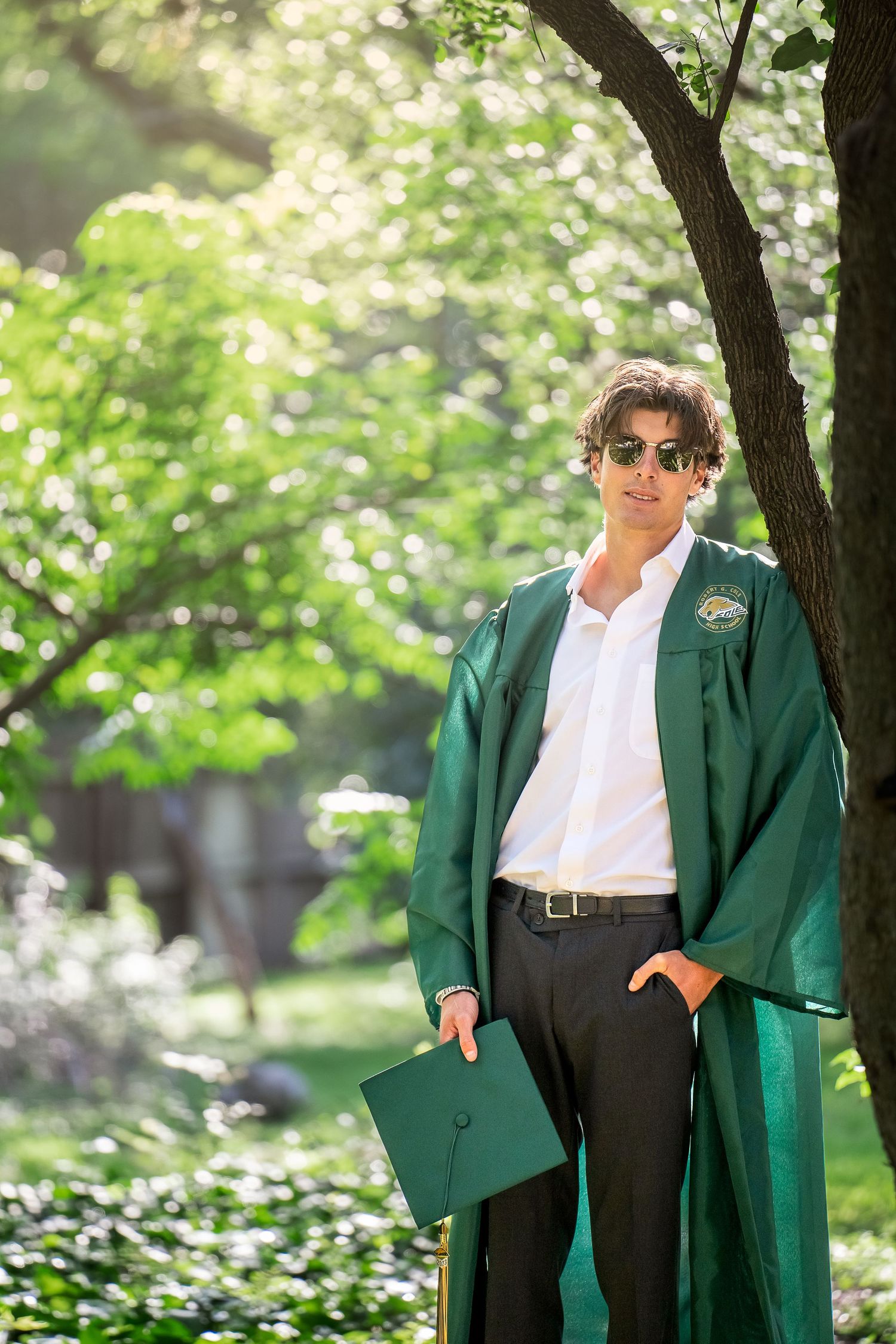 Landa Gardens at Landa Library high school senior boy in cap and gown leaning against tree