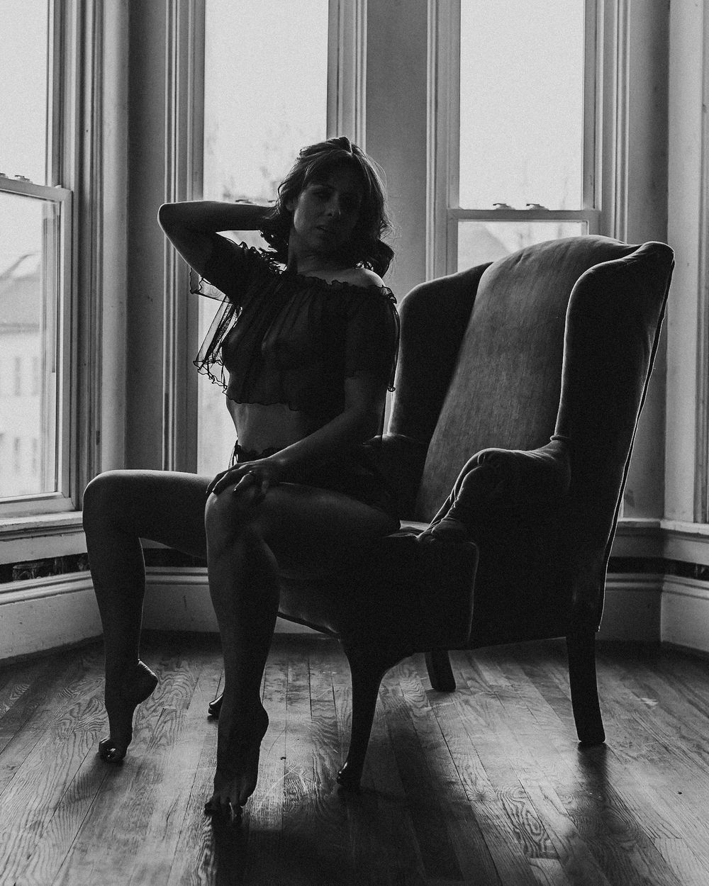 Artistic black and white photo of silhouette in vintage chair by window.