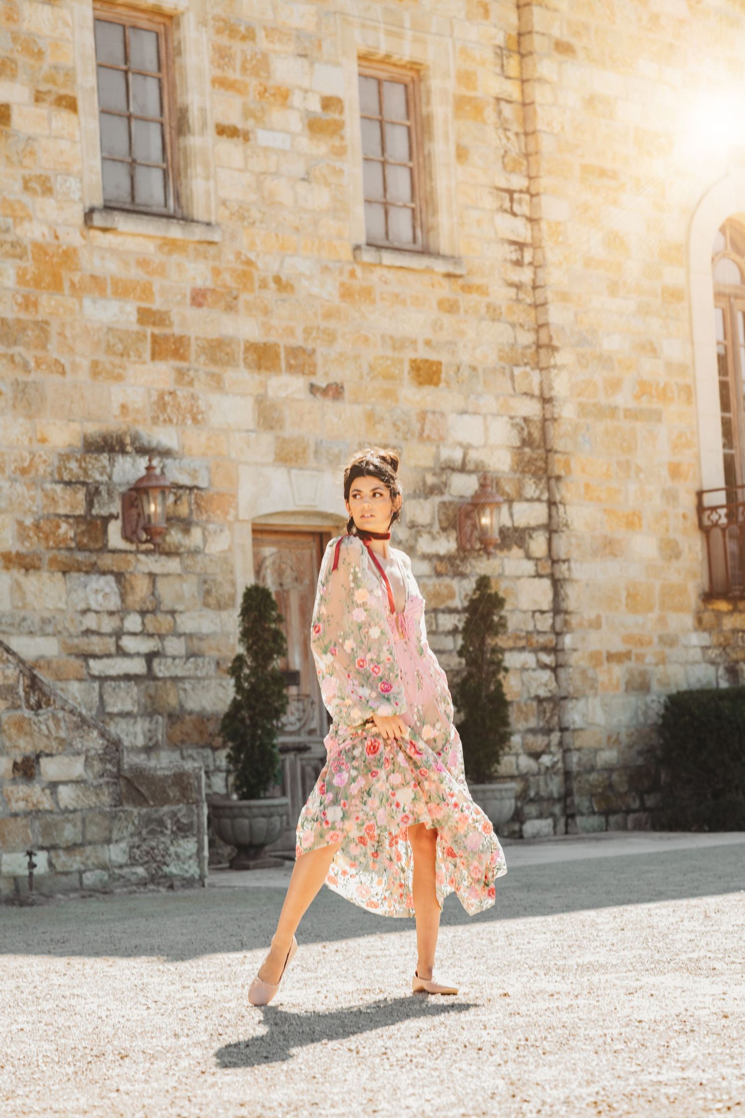 Playful movement series in floral dress against historic stone building.