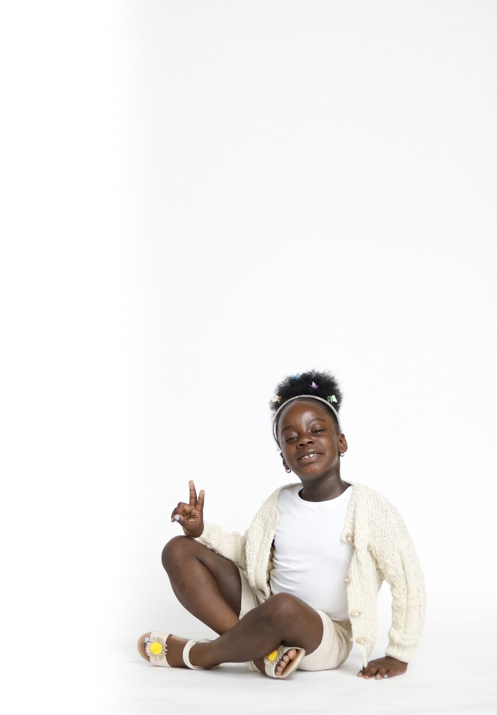 Candid lifestyle photography of child in cream outfit against white background.