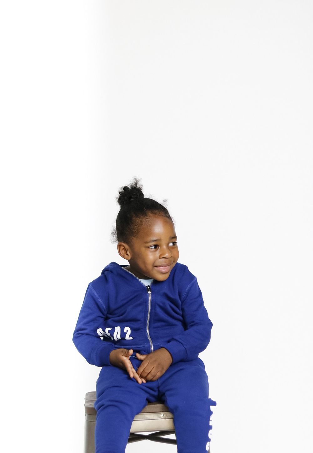 Child wearing bright blue jumpsuit posing on white backdrop.