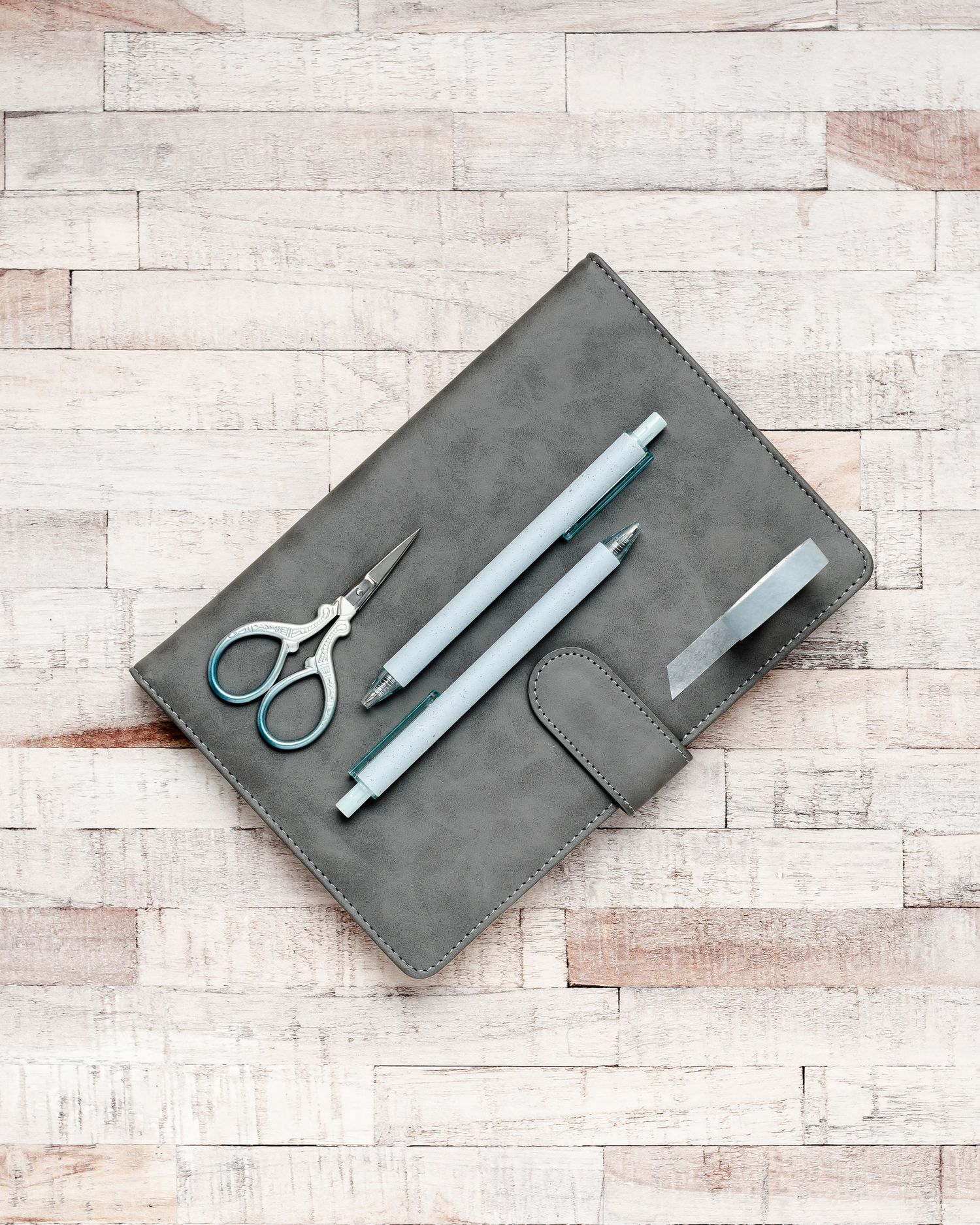 Grey journal on wooden desk flatlay with blue pens and scissors on top. Office, online business, organisation