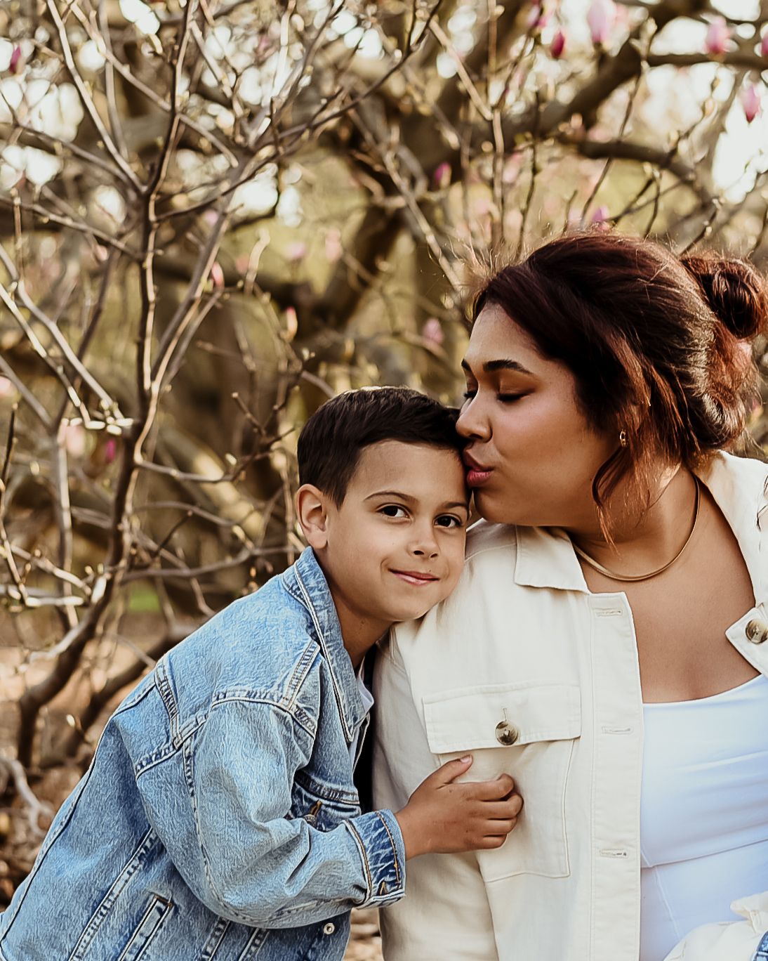 Affectionate outdoor portrait of parent and child in denim jacket against blooming spring branches.