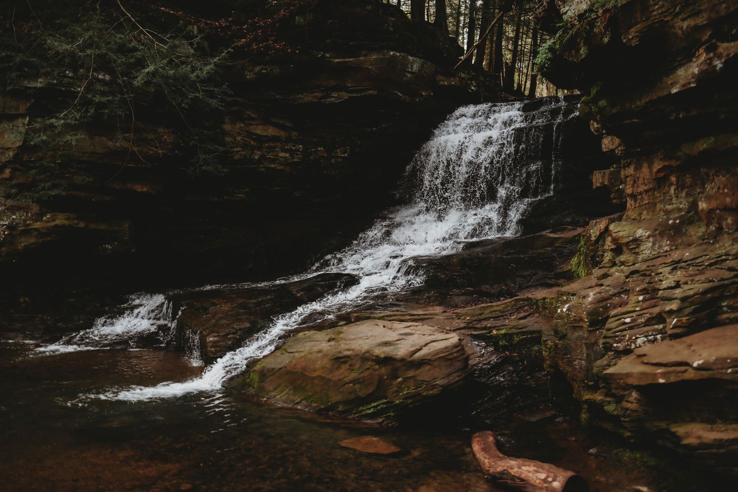 A serene waterfall cascades over rocky cliffs surrounded by autumn foliage in a peaceful forest setting.