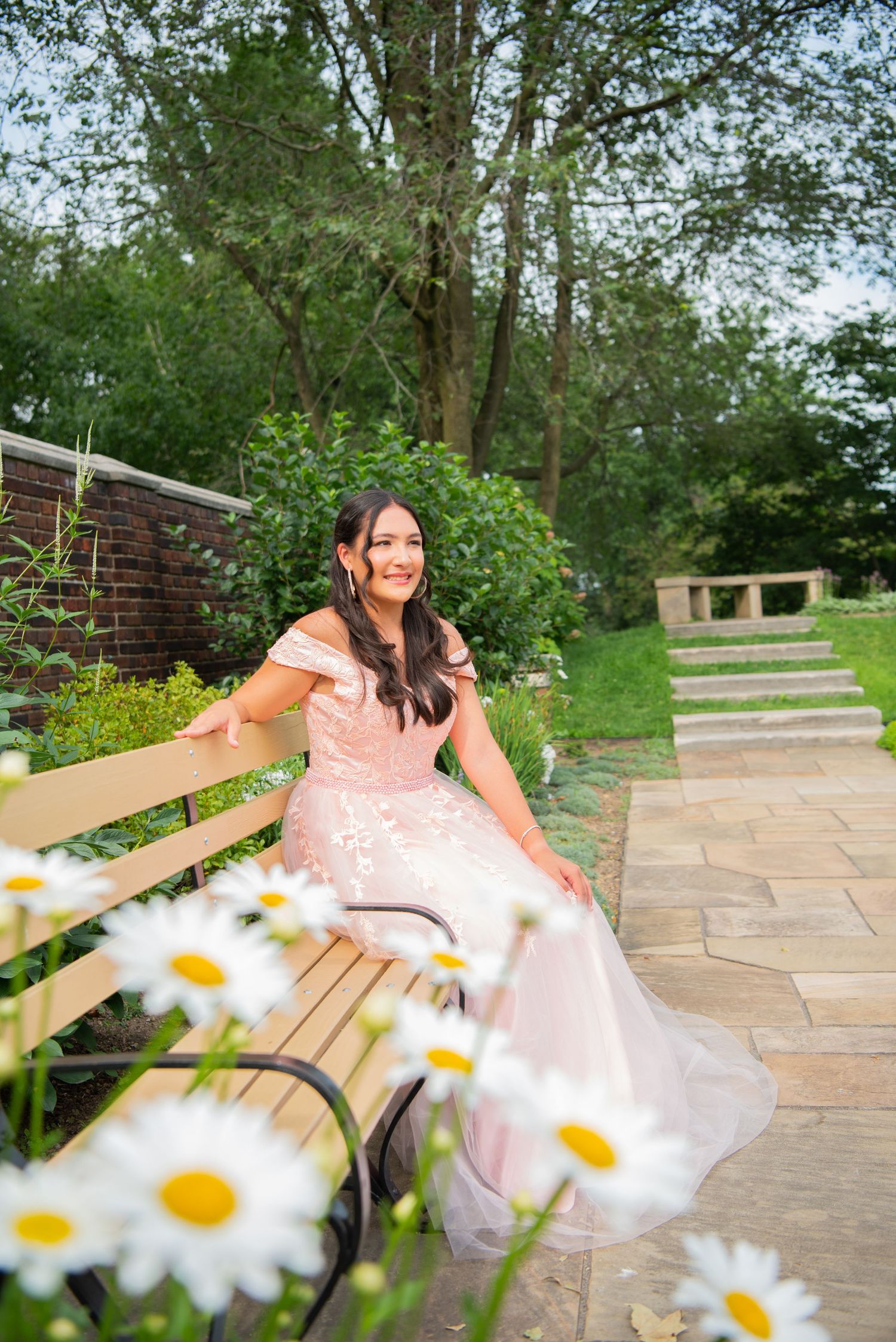 girl in pink gown seated on bench at mellon park with daisies