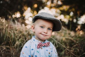 Child wearing baseball cap and button-up shirt smiles during golden hour portrait session.