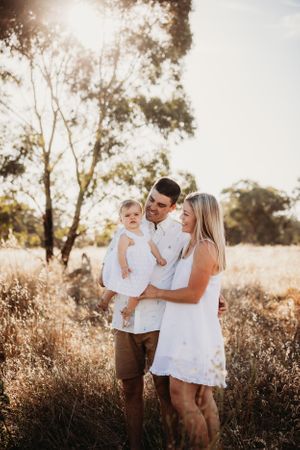Family embraces together in a golden field during sunset wearing coordinated white outfits.