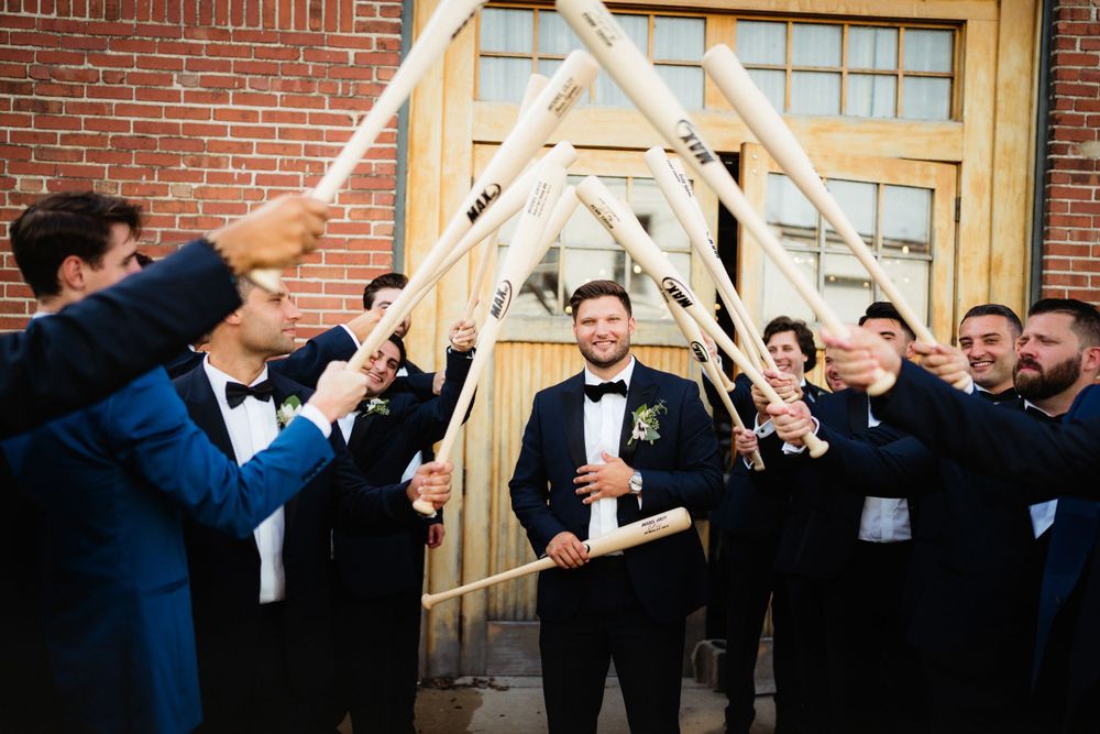 Groomsmen create an arch with drumsticks for groom in formal celebration.