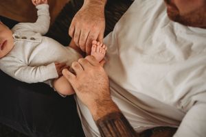 Close-up of hands gently holding a baby's tiny foot on a couch.
